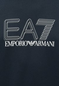 Tengerészkék pulóver fehér nyomott szöveggel: „EA7 EMPORIO ARMANI” különböző vastagságú betűkkel, logóval díszítve. Puha textúra, laza kialakítás.