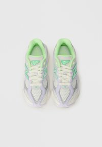 Des chaussures de sport légères avec une tige en maille blanche, des accents violets et verts ; elles présentent des semelles épaisses et un design à lacets.