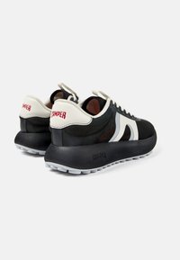 Sneakers bianco e nero con tomaia in rete, suola spessa e branding "CAMPER" sul tallone. Texture liscia con motivi a contrasto.