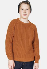 Rostfarbener, gestrickter Pullover mit strukturiertem Muster, gerippten Bündchen und Saum, rundem Halsausschnitt, getragen mit dunklen Jeans.