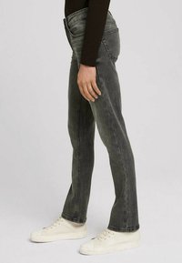 Grå denim flarejeans med hög midja och subtila blekningar, kompletterade med off-white sneakers, vilket visar en figursydd silhuett.