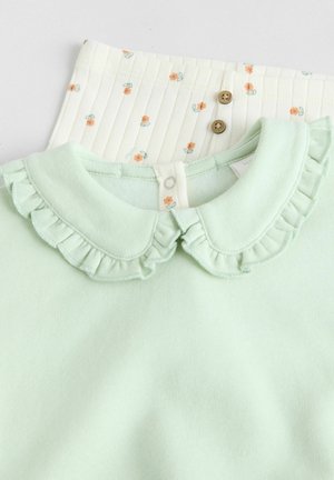 Top verde menta con colletto arricciato, abbinato a un pantalone crema con piccoli motivi floreali e bottoni in legno. Tessuto testurizzato.