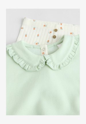 Lichtgroene top met een gerimpelde kraag, gecombineerd met een crèmekleurige onderkant met kleine bloemenpatronen en houten knopen. Getextureerde stof.