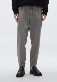 Világosszürke, kényelmes szabású nadrág rugalmas derékpánttal és húzózsinórral, finom oldalzsebekkel és sima, matt felülettel.