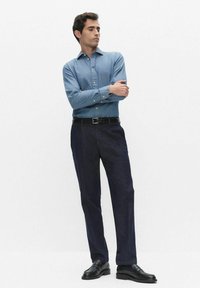 Lichtblauw overhemd met knopen, gecombineerd met donkerblauwe pantalon, uitgevoerd in een klassieke pasvorm en donkere nette schoenen. Eenvoudig, strak ontwerp.