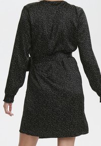 Vestido negro con mangas largas, cintura ceñida y un patrón de puntos blancos salpicados. Tela suave con un corte holgado, que termina a mitad del muslo.