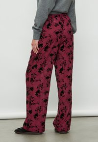 Pantaloni largi cu un model în carouri roz și accente florale negre. Fabrică moale, cu talie elastică. Pantofi negri cu talpă plată purtați.