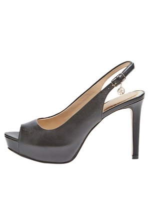 Zapato de tacón alto de piel negra tipo slingback con punta abierta, plataforma en la parte delantera y un charm metálico en la correa. Textura suave y diseño elegante.