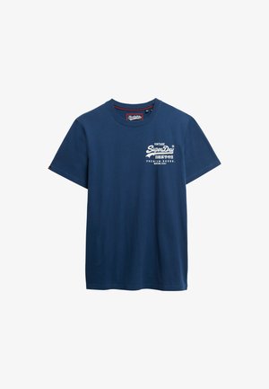 Granatowy bawełniany t-shirt z okrągłym dekoltem, krótkimi rękawami i białym nadrukiem logo na piersi. Posiada czerwony akcent wewnątrz kołnierzyka.