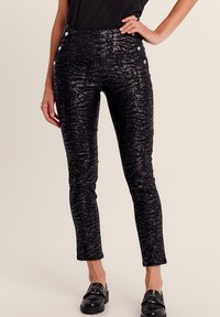 Pantaloni a vita alta neri con motivo, dotati di una leggera lucentezza, caratterizzati da bottoni decorativi in vita e gambe svasate. Texture morbida.