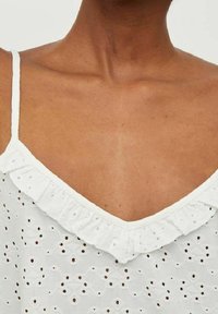Top bianco senza maniche con scollo arricciato, caratterizzato da motivi ad occhiello ricamati e un design a forma di V. Texture liscia.