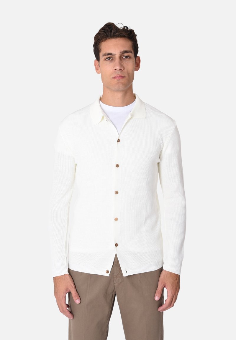 Cardigan bianco lavorato a maglia con colletto, dotato di bottoni in legno sulla parte anteriore, orlo dritto e maniche lunghe. Indossato con pantaloni beige.