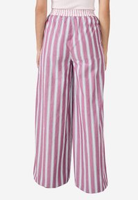 Kobieta w luźnych, wysokich spodniach w pionowe różowe, białe i niebieskie paski, pokazana od talii do stóp.