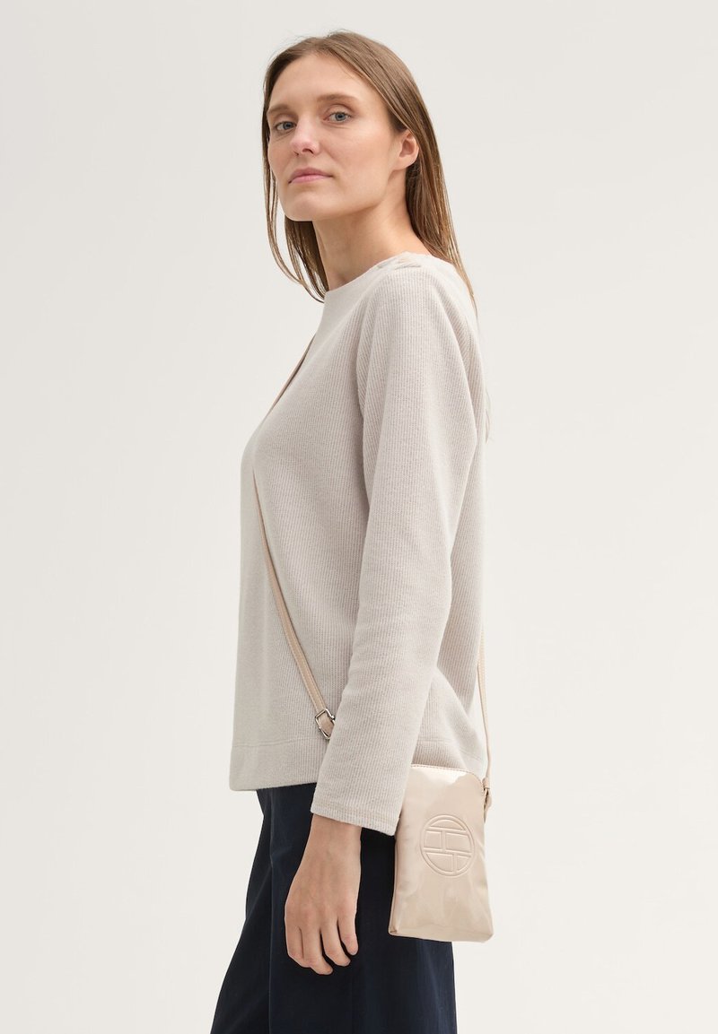 Suéter de canalé beige claro con un escote ancho y mangas largas, combinado con un pequeño bolso cruzado en color crema con un diseño circular.