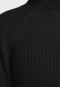 Czarny sweter z prążkowanego dzianiny z wysokim kołnierzem, wykonany z miękkiego materiału o fakturowanej powierzchni, podkreślający pionowe paski.