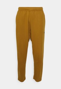 Mosterdgele sportbroek van zacht materiaal. Voorzien van een elastische tailleband en zijzakken. Klein zwart logo dicht bij de zoom.