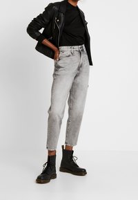 Černá kožená bunda, přiléhavý černý top, světle šedé džíny s vysokým pasem a černé kotníkové boty s šněrováním a žlutým prošíváním.