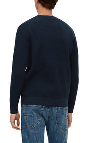 Granatowy sweter w prążki z okrągłym dekoltem, długimi rękawami i dopasowanym wykończeniem, zestawiony z jasnoniebieskimi dżinsami z tylnymi kieszeniami.