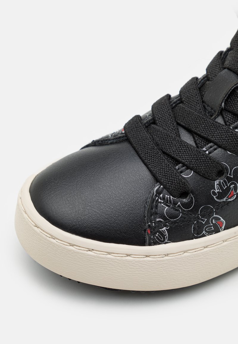Schwarze Sneaker mit dickem weißen Absatz, schwarzen Schnürsenkeln und einem dezenten Muster von Mickey-Maus-Gesichtern entlang der Seite.