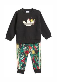 Juodas džemperis su gėlėtu Adidas logotipu, derinamas su juodomis kelnėmis su gėlių raštu, kuriomis dengtos žalios, raudonos ir geltonos gėlės bei auksinės detalės.