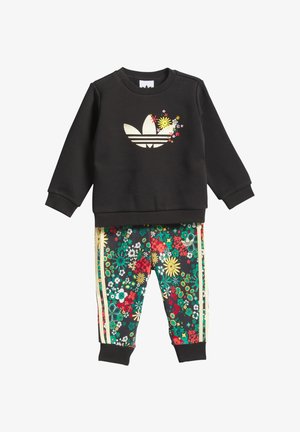 Camisola preta com logótipo floral da Adidas, combinada com calças pretas com padrão floral contendo flores verdes, vermelhas e amarelas, com detalhes em dourado.