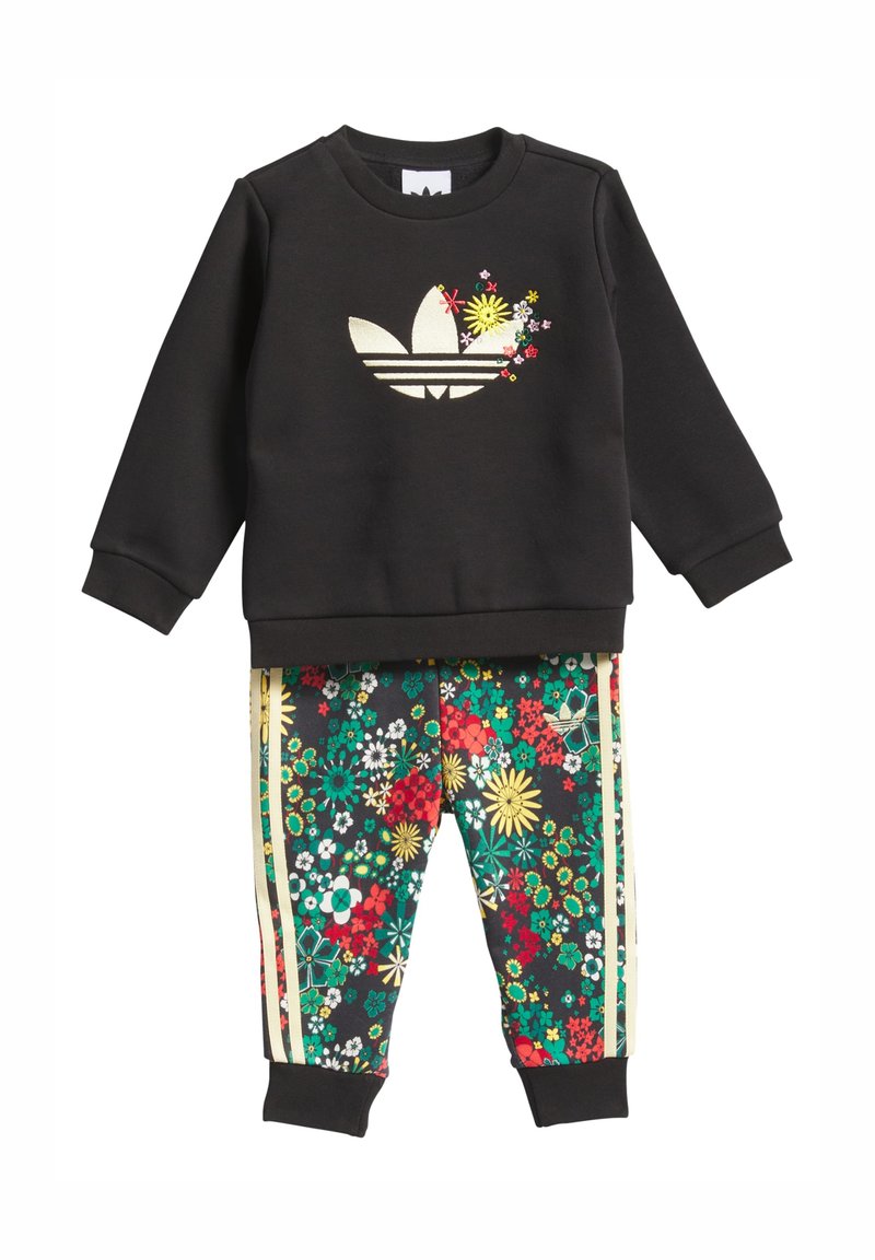 Juodas džemperis su gėlėtu Adidas logotipu, derinamas su juodomis kelnėmis su gėlių raštu, kuriomis dengtos žalios, raudonos ir geltonos gėlės bei auksinės detalės.