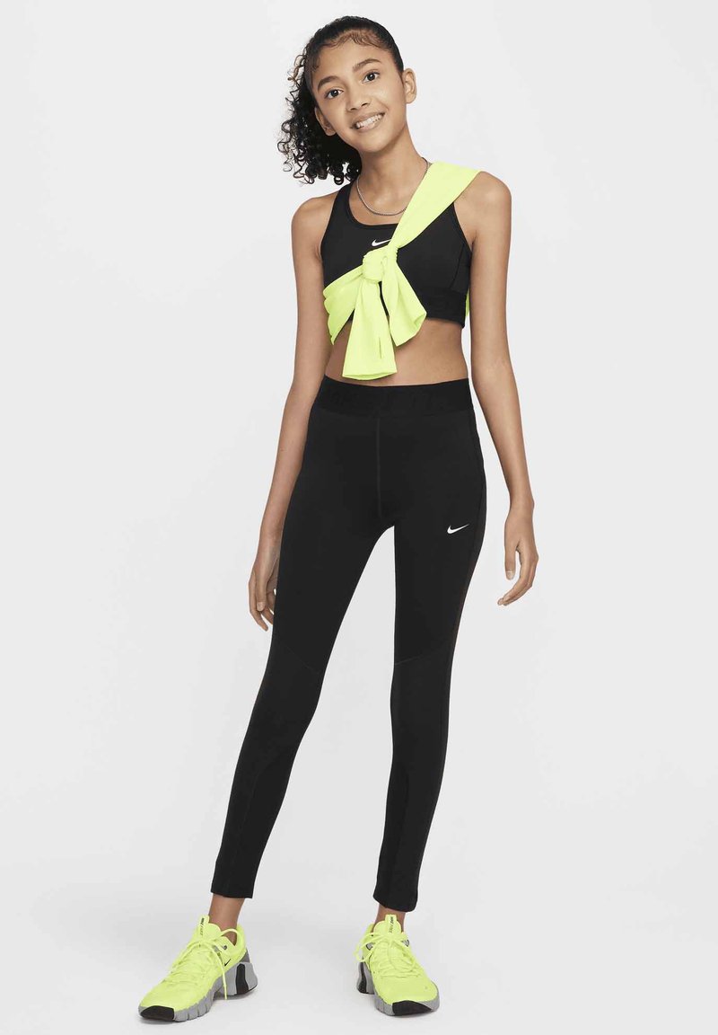 Top corto atletico nero con un vivace dettaglio a nodo giallo, abbinato a leggings neri e sneakers giallo brillante.