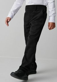 Schwarze maßgeschneiderte Hose aus strukturiertem Stoff, gerader Schnitt und mit seitlichen Taschen, kombiniert mit schwarzen Sneakers und einem weißen Langarmshirt.