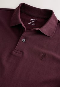 Burgundské polo tričko slim střihu z texturované látky, s límečkem, tříknopovou légou a jemně vyšitým logem na prsou.