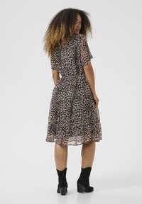  Leopardi mustriga kleit lühikeste varrukatega, vööl peenike, voolav seelik ja õhuline tekstuur, kombineeritud mustade pahklöökidega kingadega.