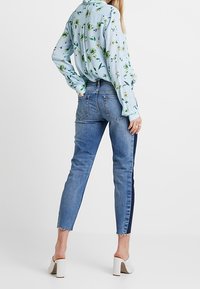 Ljusblå blommig blus, åtsittande blå jeans med en mörk sidremsa, fransad fåll och vita blockklackskor.