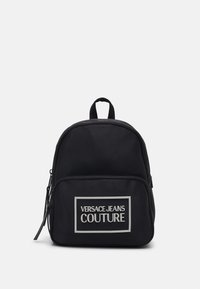 Svart nylonryggsäck med rundad form har en zippered framficka, handtag på toppen och en tydlig grafisk logotyp på framsidan.