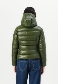 Groene, gewatteerde jas met een glanzende afwerking en een capuchon. Heeft horizontale gestikte secties en is gecombineerd met blauwe spijkerbroeken.