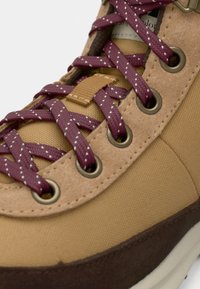 Zapatillas de deporte color tan con una parte superior de tela, suela de goma marrón y cordones de lunares color marrón. Ojetes metálicos notables que mejoran la durabilidad.