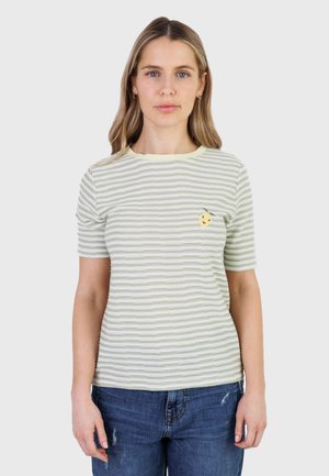 Kvinde med skulderlangt blondt hår iført lysegrøn og hvide stribede kortærmede skjorte med gult smiley-ansigt emblem og blå jeans.