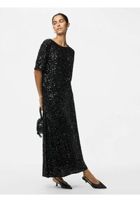 Sort, pailletteret maksikjole med korte ærmer og rund halsudskæring. Kombinationen inkluderer sorte spidse slingback-sko og en lille sort håndtaske.