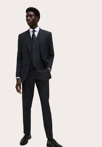 Tailored dark grey suit featuring a three-piece design with a notch lapel, slim-fit trousers, and smooth fabric. Paired with a white shirt and dark tie.