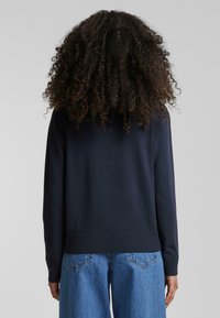 Marineblå strikkegenser med ribbestrikkede ermer og kant, med en avslappet passform og en glatt tekstur. Kombinert med lyseblå denimjeans.