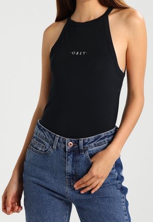 Czarny bezrękawnik z wysokim dekoltem i białym logo "OBEY" na środku klatki piersiowej, zestawiony z niebieskimi dżinsami z wysokim stanem.