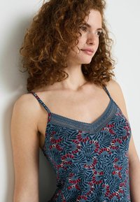 Camisola floreale blu con accenti rossi, spalline regolabili, rifinitura in pizzo lungo il décolleté, realizzata in un tessuto liscio e testurizzato con motivi a foglia.