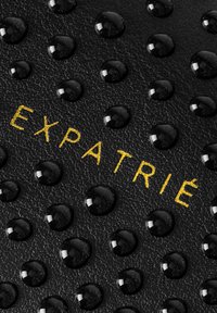 Fekete textúrájú bőr, fényes fekete cseppjekkel és arany betűkkel, amelyek középen kiemelve az "EXPATRIÉ" szót mutatják.