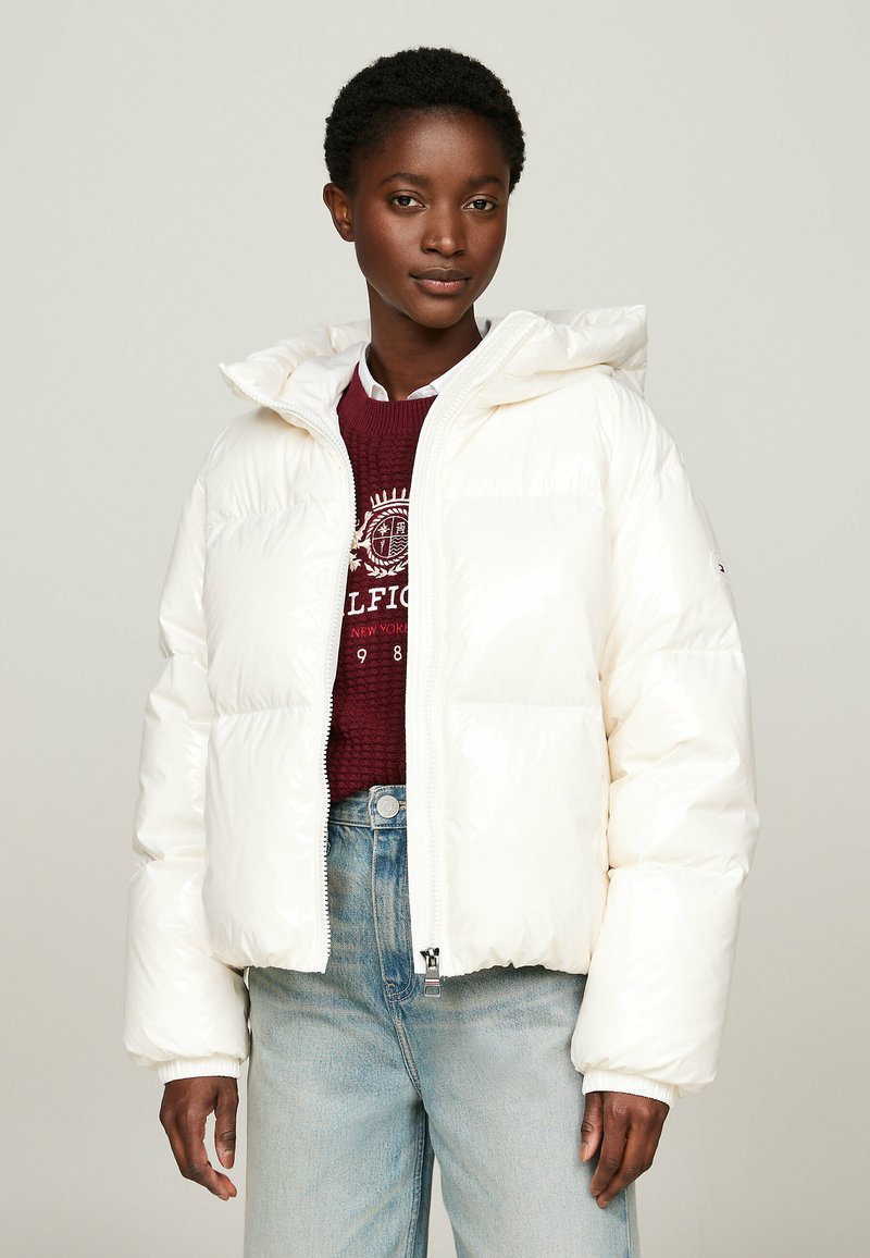 White puffer jacket with a hood, featuring a zip front, ribbed cuffs, and smooth, shiny fabric. Worn over a burgundy knit sweater and denim.
