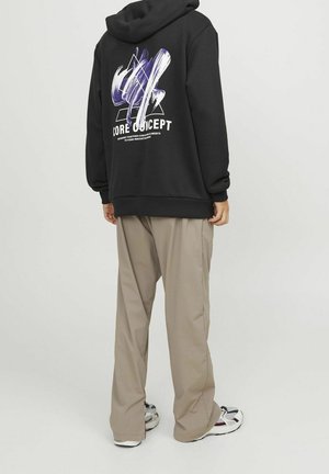 Sweat à capuche noir avec un motif blanc et violet au dos, associé à un pantalon beige clair et des baskets multicolores, présentant une coupe ample.