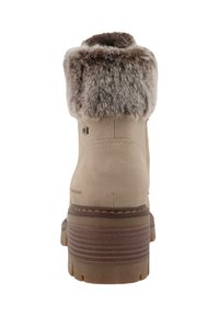 Botte au cheville en fausse fourrure beige, avec une surface texturée, un bout rond et une semelle en caoutchouc brun robuste présentant des rainures horizontales.