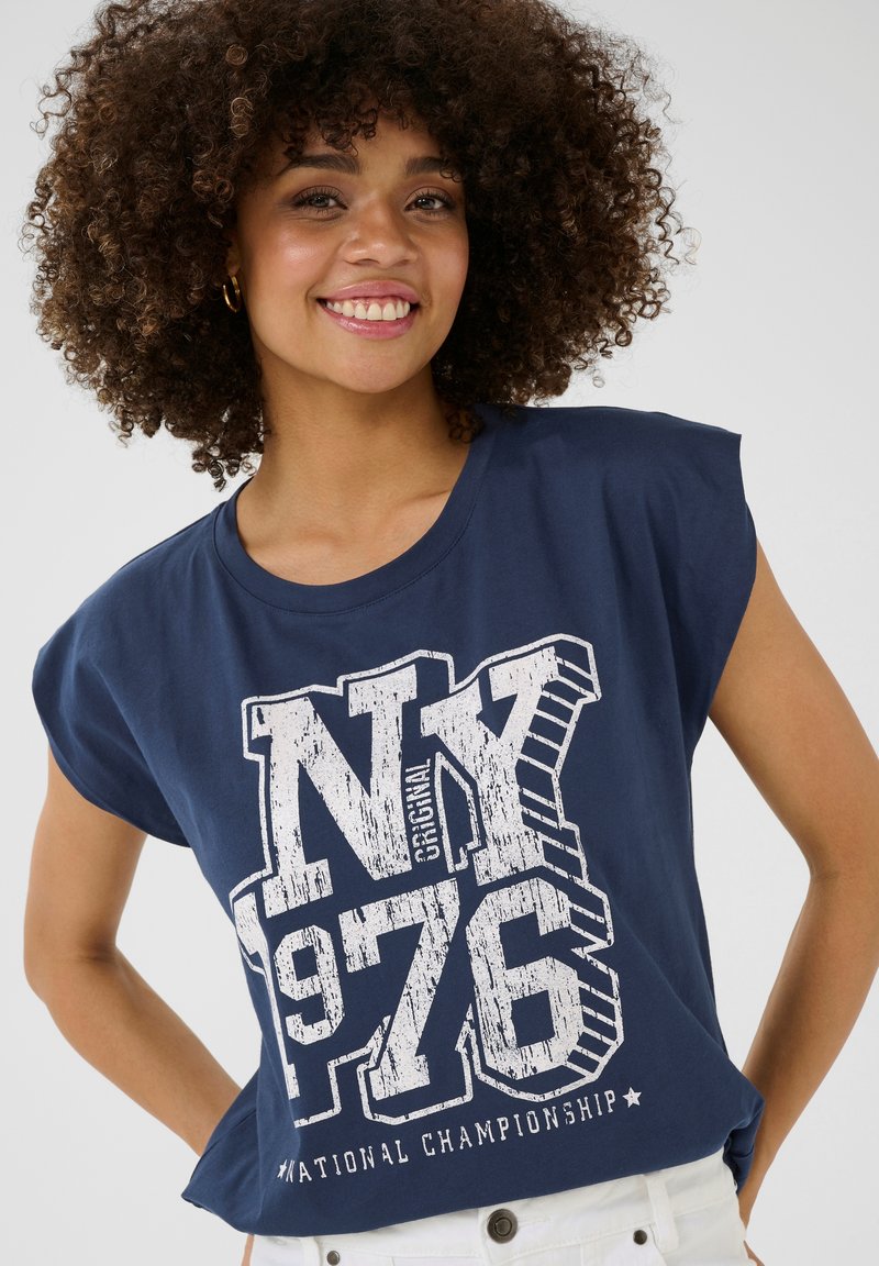 Tumši zila īsām piedurknēm t-krekls, izgatavots no kokvilnas, ar baltu grafisku apdruku, kurā ir teksti "NY 1976" un "Nacionālā čempionāta".