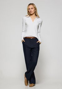 Vit långärmad skjorta med krage, matchad med marinblå byxor och ett brunt bälte; beige läderskor fulländar outfiten.