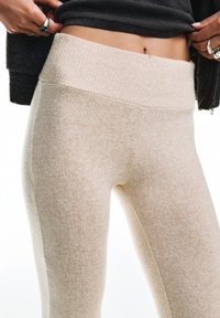 Bézs leggings bordázott derékrésszel és sima textúrával, testhezálló szabással és oldalsó varrásokkal. Az anyag puhanak és rugalmasnak tűnik.