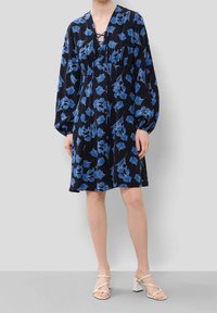 Námořnické šaty s květinovým modrým vzorem, výstřihem do V a nafouknutými rukávy. Tkanina je hladká; zahrnuje detail šněrování vpředu.