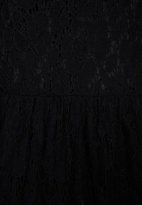 Svart spetstyg med intrikata blommönster, med en texturerad yta och ett volangavslut nederst för extra detalj.