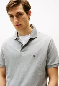Grijze polo shirt van zachte stof, met een klassieke kraag, een drie-knopenpad en een klein logo met rode, witte en blauwe accenten.